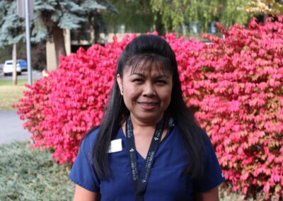 smiling care giver standing before vibrant red bush